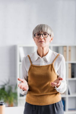 Orta yaşlı takım lideri yerinde duruyor ve el kol hareketi yapıyor.
