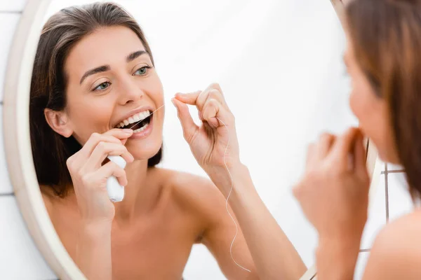 Młoda Kobieta Patrząc Lustro Podczas Nici Dentystycznej Zębów Łazience Rozmyty — Zdjęcie stockowe