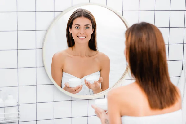 Feliz Joven Mujer Sosteniendo Crema Cosmética Cerca Del Espejo Baño —  Fotos de Stock