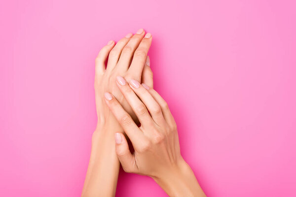 верхний вид ухоженных женских рук с блестящими ногтями на розовом фоне
