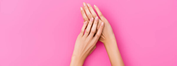 верхний вид женских рук с ногтями покрыты пастельным лаком для ногтей на розовом фоне, баннер