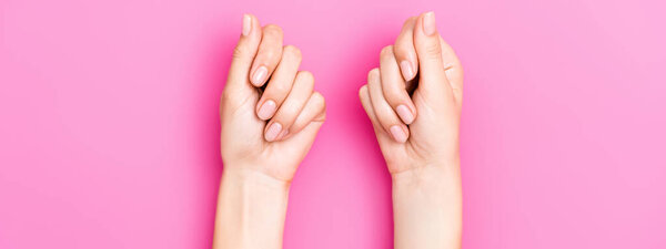 верхний вид женских рук с пастельной эмалью на ногтях на розовом фоне