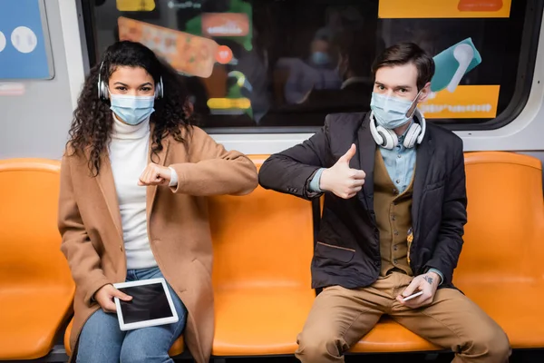 Pareja Interracial Máscaras Médicas Golpeando Codos Sosteniendo Gadgets Metro — Foto de Stock