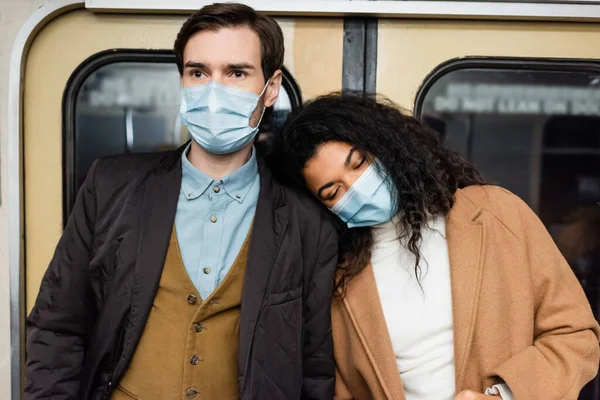 african american woman in medical mask leaning on boyfriend in subway