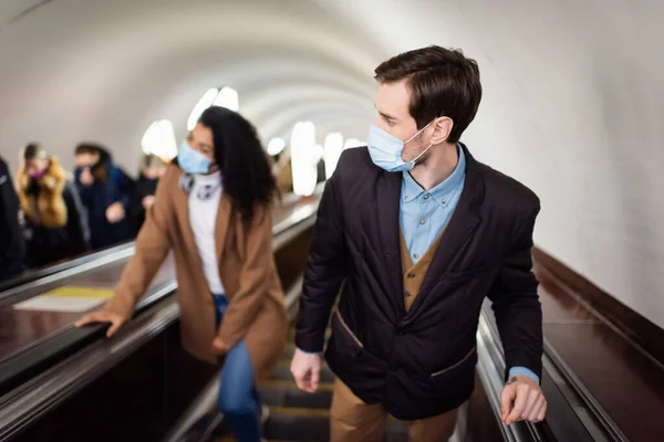 Mann Mit Medizinischer Maske Steht Auf Rolltreppe Neben Afroamerikanerin Vor — Stockfoto