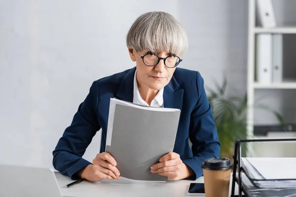 Medelålders Gruppledare Glas Som Håller Mapp Nära Prylar Och Pappersmugg — Stockfoto