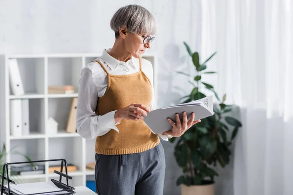 mature team leader in glasses holding folder with documents and contract