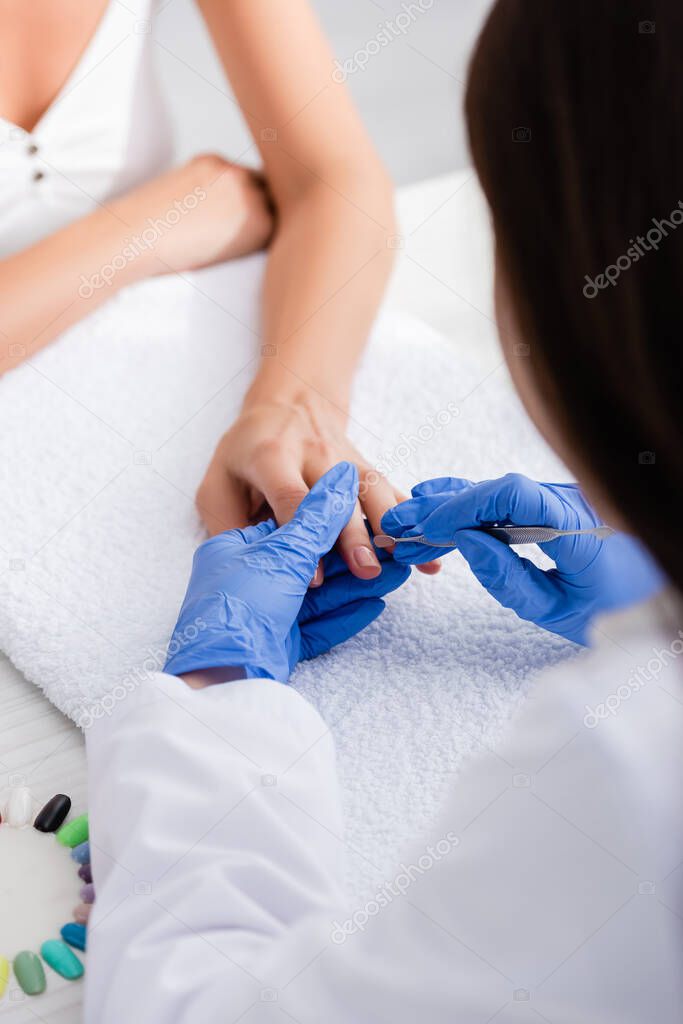 partial view of manicurist making manicure to client with cuticle pusher, selective focus