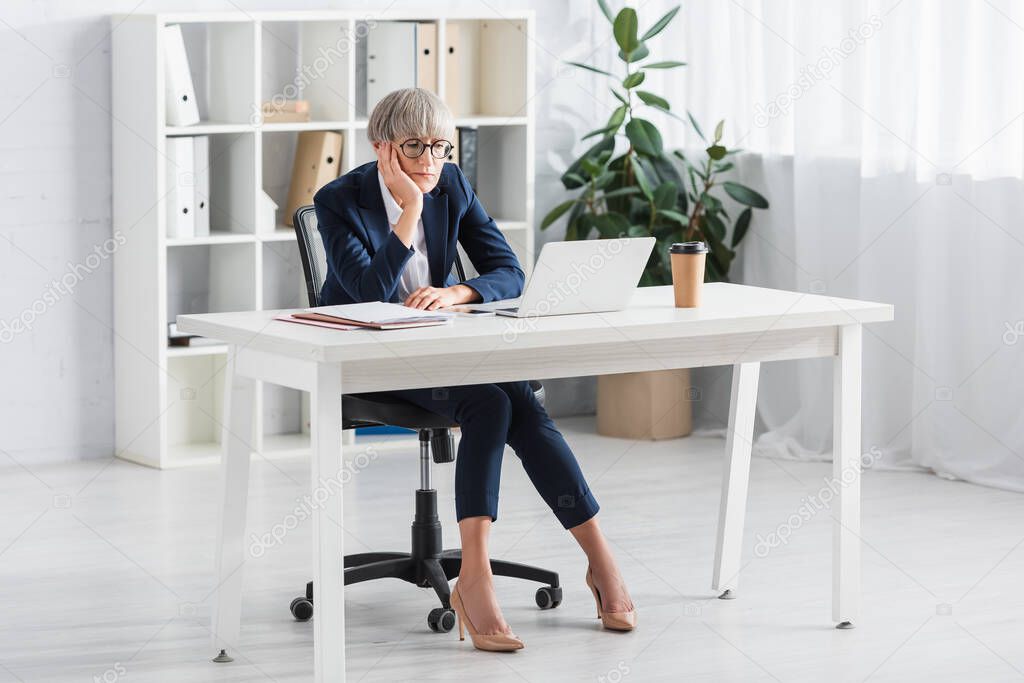 bored team leader in glasses looking at laptop in modern office