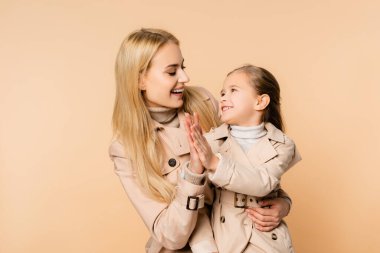 Neşeli sarışın anne ve gülümseyen kız bejde beşlik çakıyor.