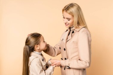 Şefkatli anne ve kız el ele tutuşup birbirlerine bej rengi elbiseyle bakıyorlar.