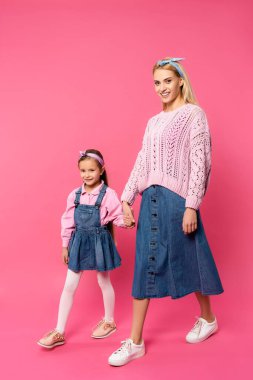 El ele tutuşurken ve pembe üzerinde yürürken gülümseyen anne ve kız.