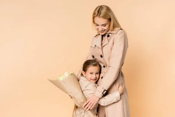 Mãe Feliz Segurando Flores Abraçando Filha Alegre Isolada Bege — Fotografia de Stock