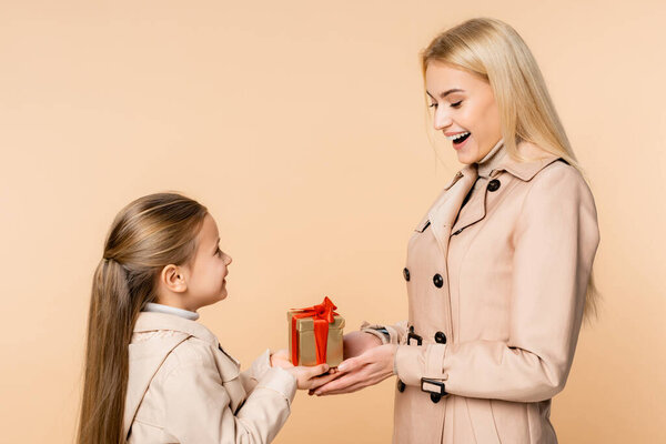 cheerful kid giving present to amazed mother on 8 march isolated on beige