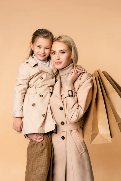Smiling Mother Holding Paper Bags Hugging Daughter Isolated Beige — Stock Photo, Image