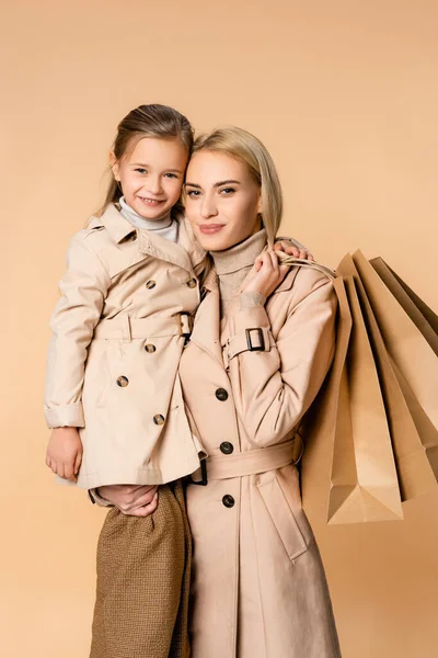 Sonriente Madre Sosteniendo Bolsas Papel Abrazando Hija Aislada Beige — Foto de Stock