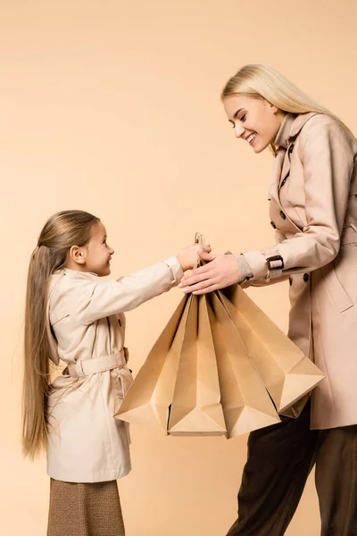 Sonriente Madre Tomando Bolsas Papel Cerca Alegre Hija Aislado Beige — Foto de Stock