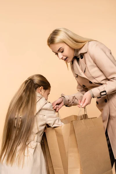 Curioso Niño Mirando Bolsas Papel Manos Madre Asombrada Aislada Beige — Foto de Stock