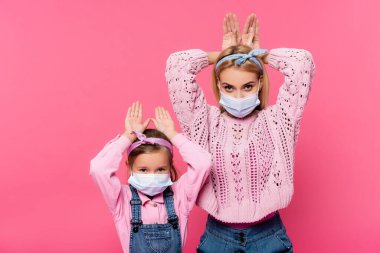 Tıbbi maskeli anne ve kızı pembe ellerle tavşan kulağı yapıyorlar. 