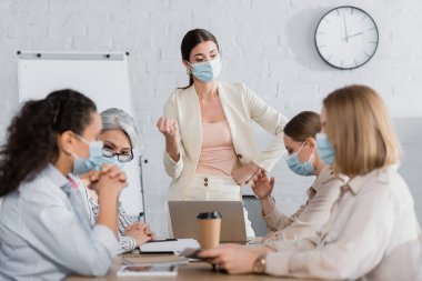 team leader in medical mask near multicultural coworkers during meeting clipart