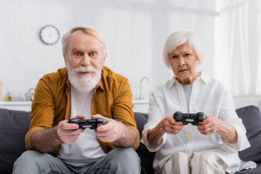 KYIV, UKRAINE - DECEMBER 17, 2020: Elderly couple playing video game at home  clipart