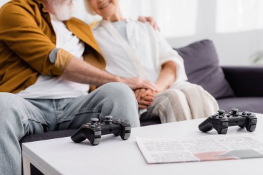 KYIV, UKRAINE - 17 ARALIK 2020: Arka planda bulanık arka planda yaşlı bir çiftin yanındaki sehpanın yanındaki kahve masasının üzerinde kesilmiş joystickler ve gazete manzarası 