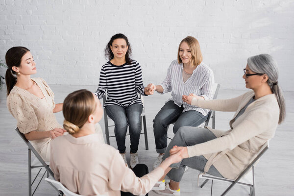 happy multicultural women smiling and holding hands during seminar 