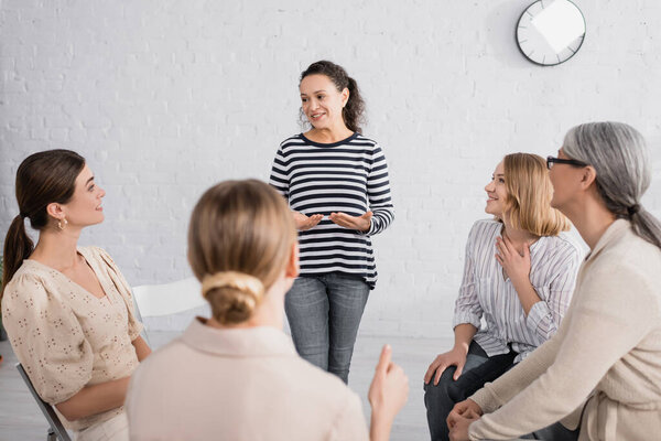 happy african american speaker standing during seminar near group of women on blurred foreground 