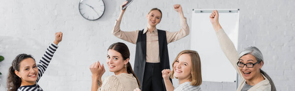 happy interracial businesswomen and speaker with raised hands during lecture, banner