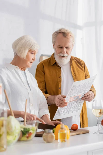 Coppia Anziana Che Legge Notizie Mentre Cucina Primo Piano Sfocato — Foto Stock