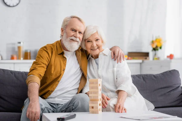 Uomo Anziano Abbracciare Moglie Vicino Blocchi Gioco Legno Telecomando Giornale — Foto Stock