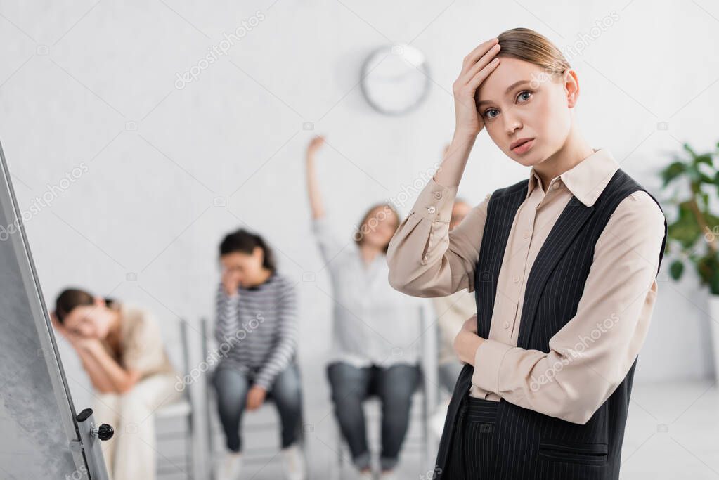 worried young speaker near businesswomen during seminar on blurred background 