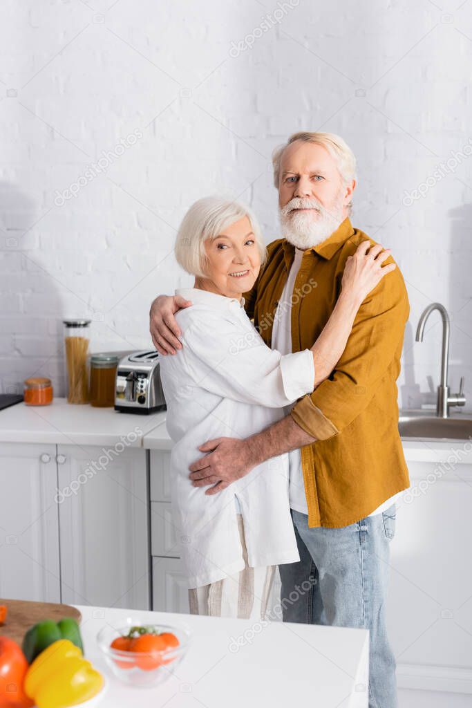 Elderly couple embracing near fresh vegetables on blurred foreground 