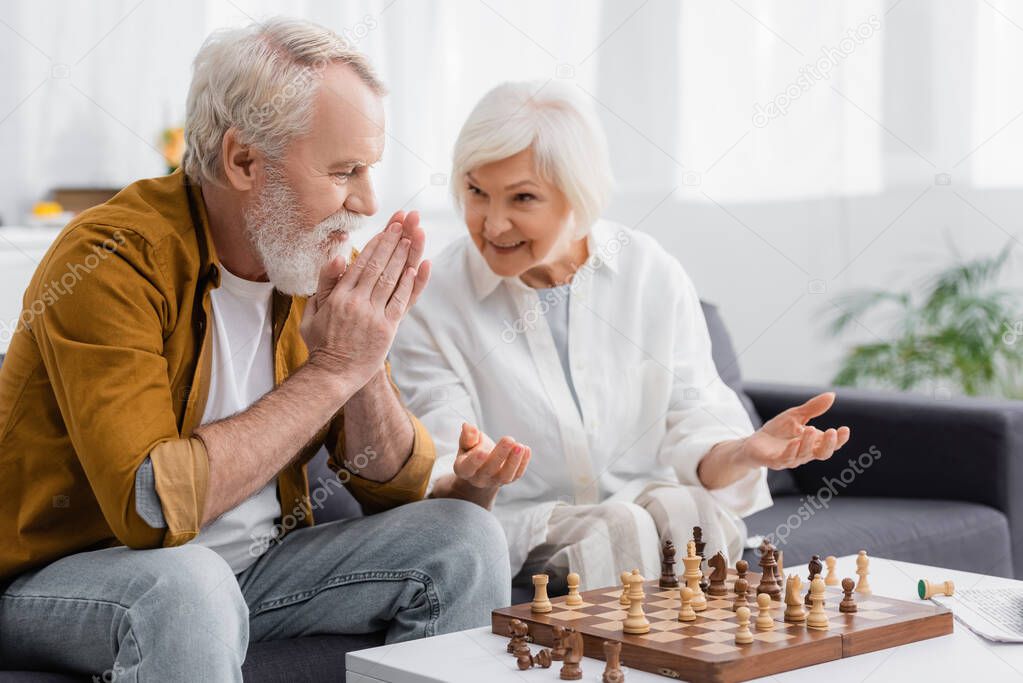 Senior man looking at chess near smiling wife on blurred background 