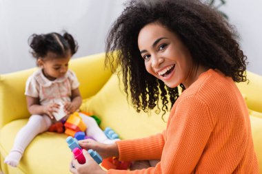 Mutlu Afro-Amerikan annesi bulanık arka planda bebekle bina blokları oynuyor.