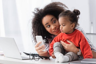 Afrikalı Amerikalı anne masada akıllı telefonu kızına gösteriyor.