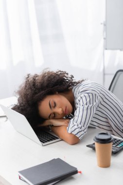 tired african american woman sleeping on laptop at home clipart