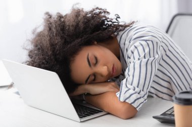 exhausted african american woman sleeping on laptop at home clipart