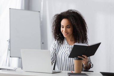 Mutlu Afro-Amerikan serbest çalışanı evden çalışırken elinde not defteri tutuyor.