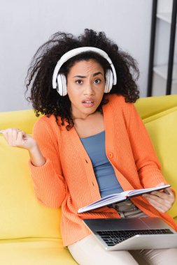 Afro-Amerikan kadın elinde defter ve kulaklıkla podcast dinliyor.