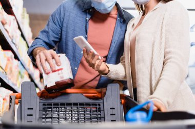 Medikal maskeli bir kadının elinde akıllı telefon paketli ve markette tramvayla sevgilisinin yanında durduğu görüntüler. 