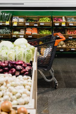 Süpermarkette taze sebzelerin yanındaki alışveriş arabası bulanık ön planda. 