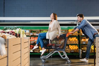 Neşeli çift markette marketin yakınındaki alışveriş arabasında takılıyor. 