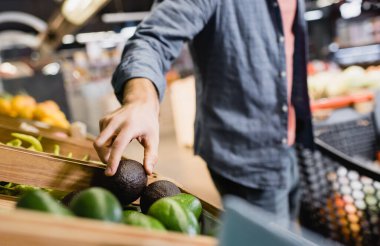 Bulanık arka planda süpermarketteki tezgahtan avokado alan bir adam görüntüsü 