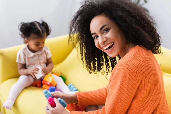 快乐的非洲裔美国母亲在模糊的背景下和蹒跚学步的孩子玩积木游戏 — 图库照片