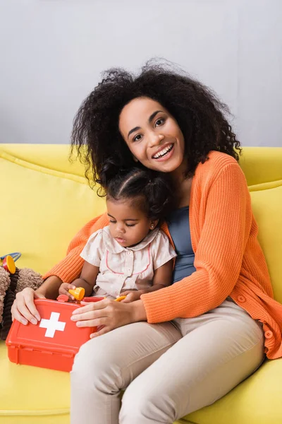 Sonriente Madre Afroamericana Sentada Con Hija Pequeña Sosteniendo Kit Primeros —  Fotos de Stock