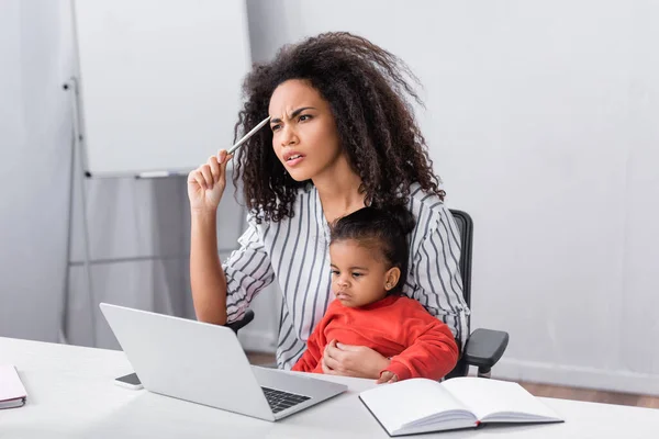 Pensativo Africano Americano Madre Sentado Con Niño Hija Mientras Trabajo —  Fotos de Stock