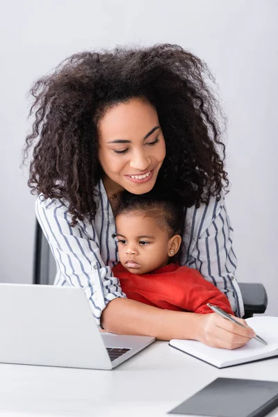 Feliz Madre Afroamericana Sentada Con Hija Pequeña Mientras Escribe Portátil — Foto de Stock