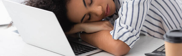 tired african american woman sleeping on laptop at home, banner