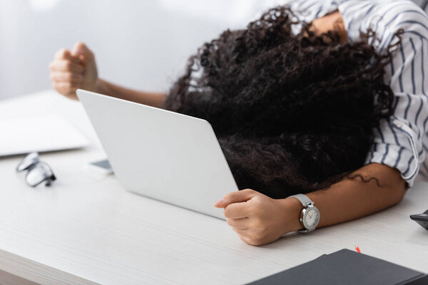 african american woman covering face while lying on laptop at home